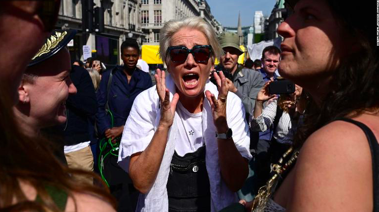 Woman wearing a white T-shirt and wearing sunglasses, shouts during a demonstration on a crowed street.