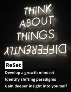 White neon sign on black background with the words, Think About Things Differently. The lettering of differently, is upside down and backward. Other text says ReSet, Develop a growth mindset, Identify shifting paradigms, Gain deeper insight into yourself