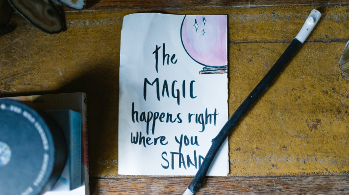 Antique table top with a paper that says, The Magic happens right where you stand".