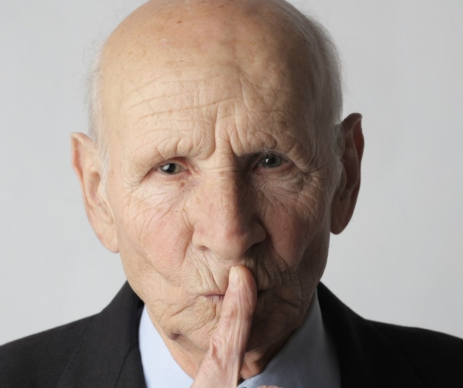 Head shot of older man with finger in front of his lips in s "shhhhh" motion.